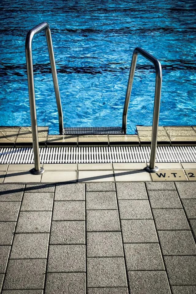 Poolside paver deck with steel handrails beside a swimming pool