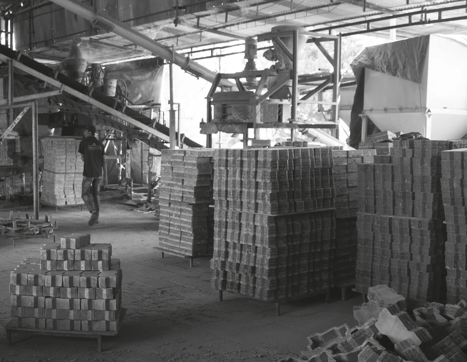 Milestone factory floor with a mixing plant, conveyor and stacked paver blocks